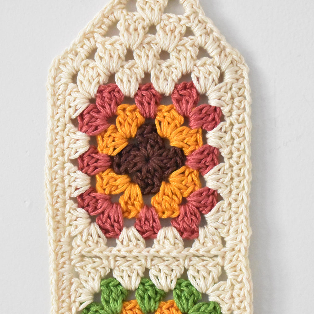 Crocheted wall hanging with a colorful granny square design on a white background.