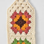 Crocheted wall hanging with a colorful granny square design on a white background.
