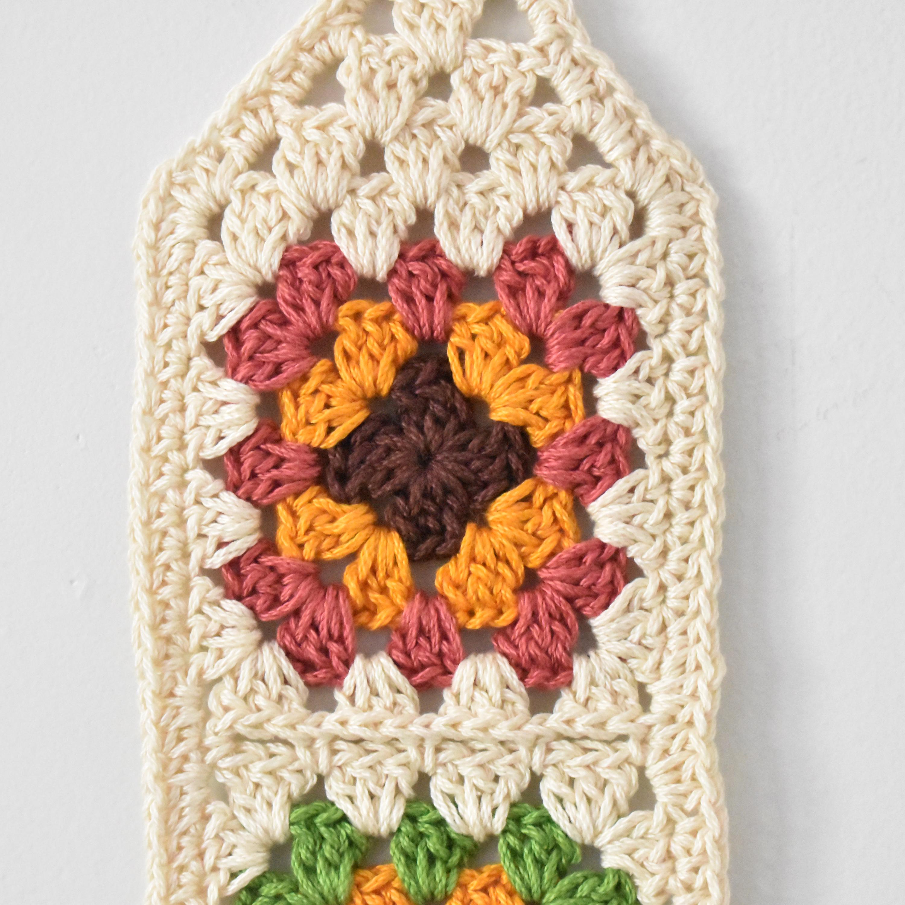 Crocheted wall hanging with a colorful granny square design on a white background.