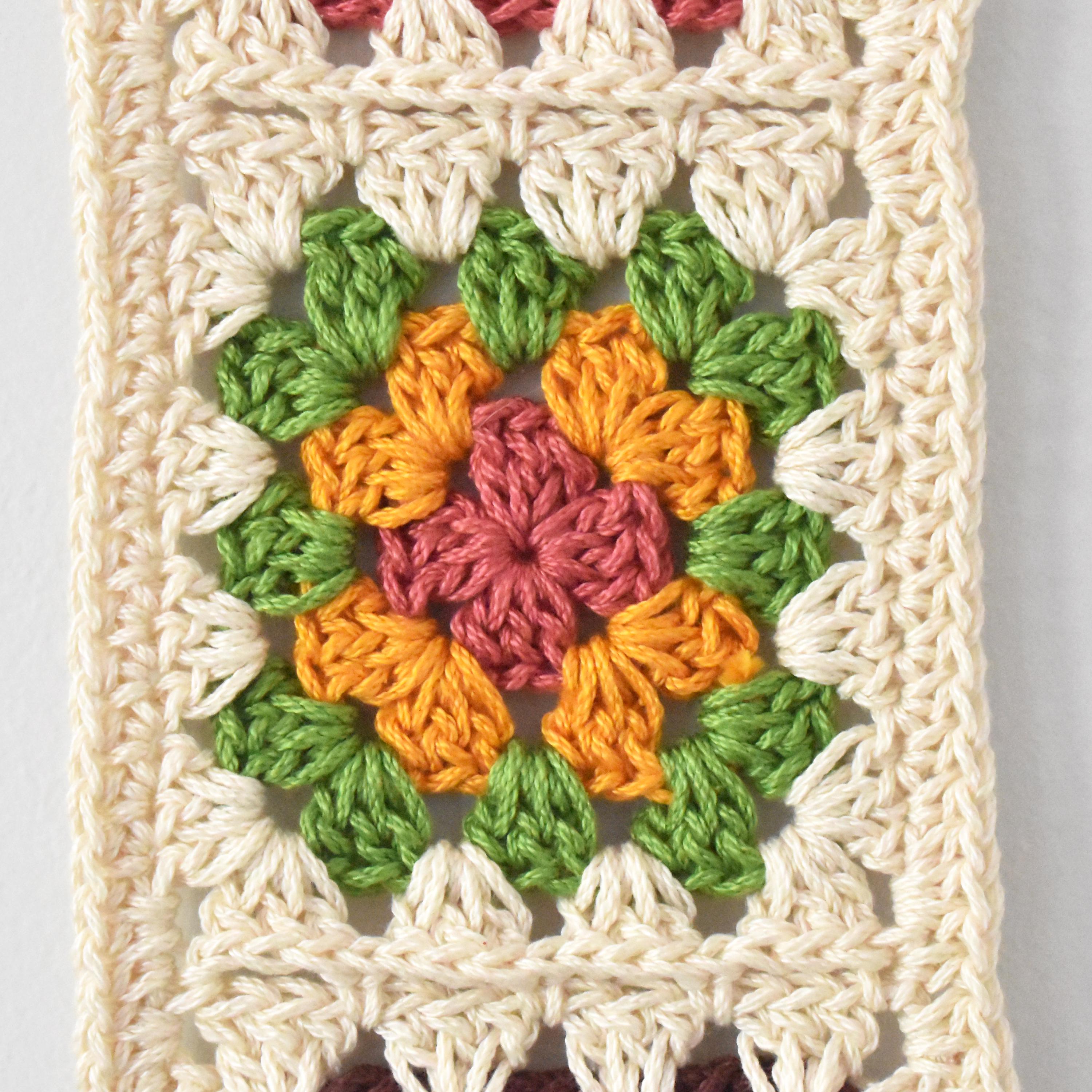 Crocheted wall hanging with a colorful granny square design on a light gray background.