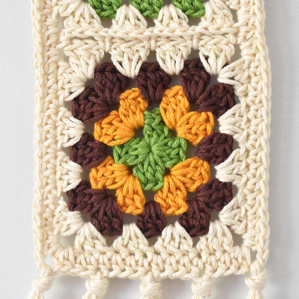 Crocheted wall hanging with a colorful granny square design on a light gray background.
