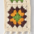 Crocheted wall hanging with a colorful granny square design on a light gray background.