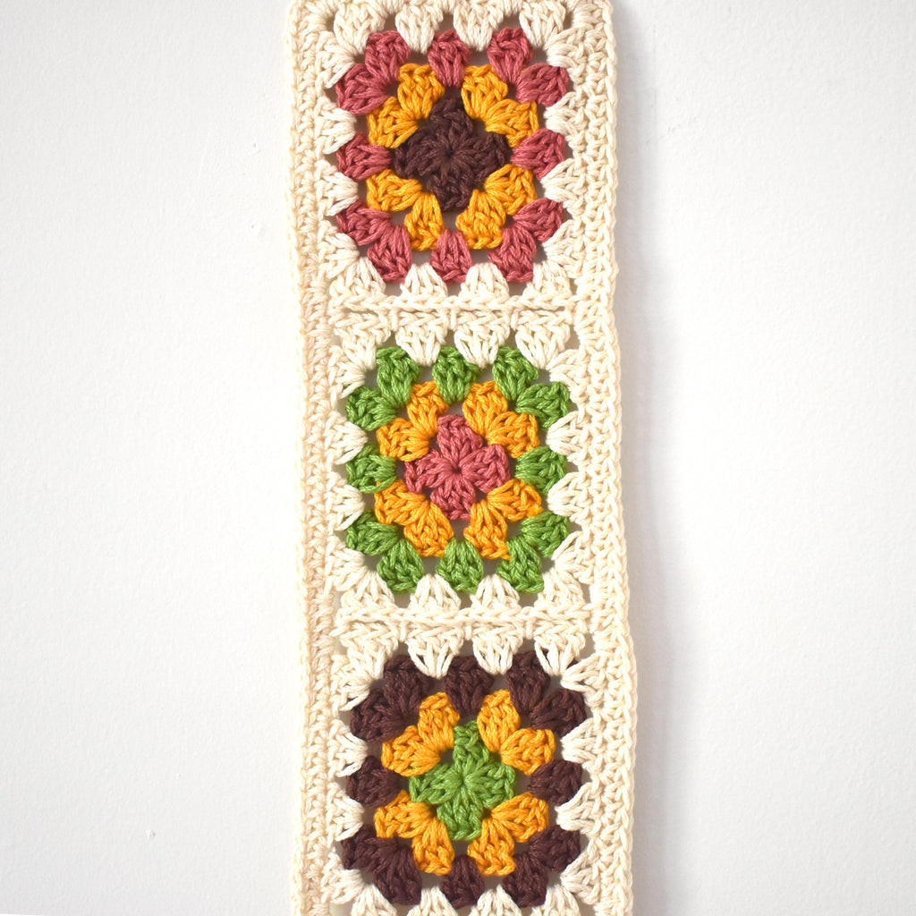 Crocheted granny square wall hanging on a white background.