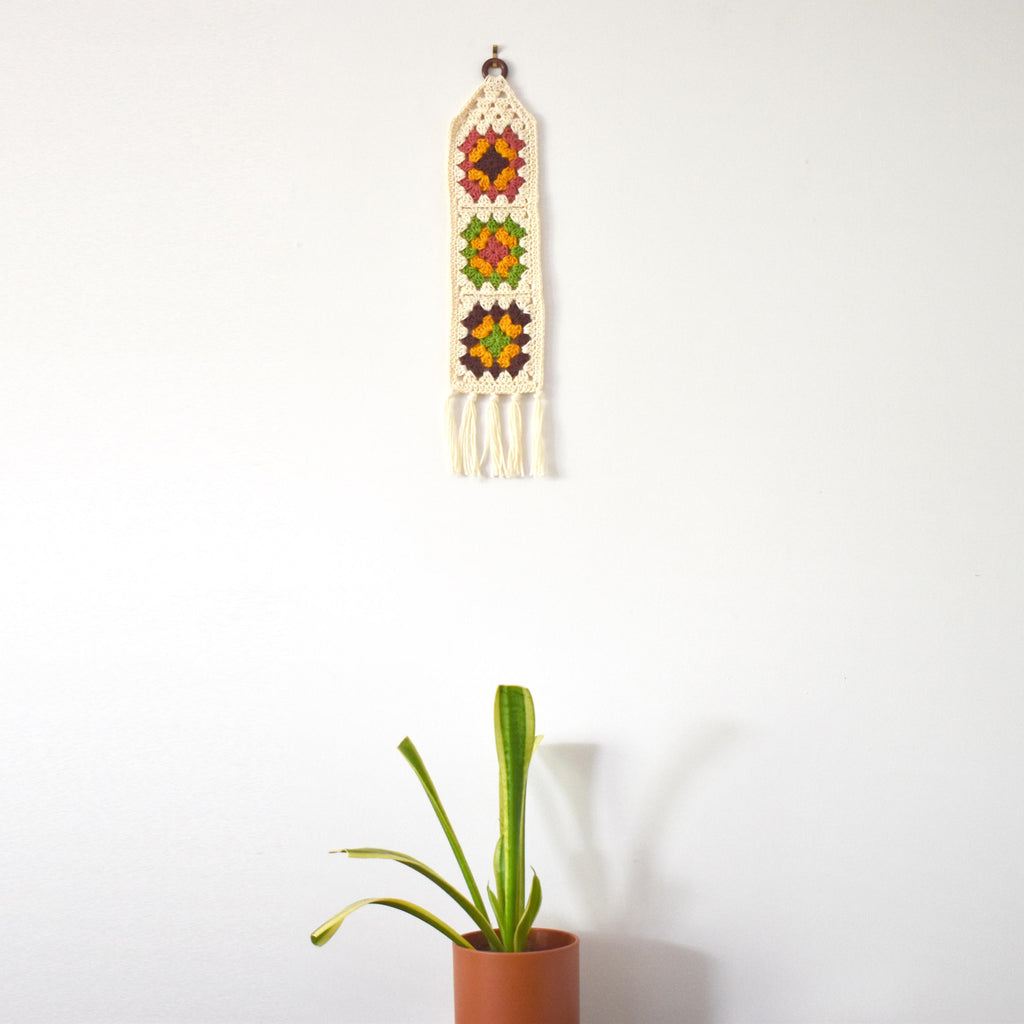 Decorative wall hanging with geometric granny square patterns and tassels on a white background.