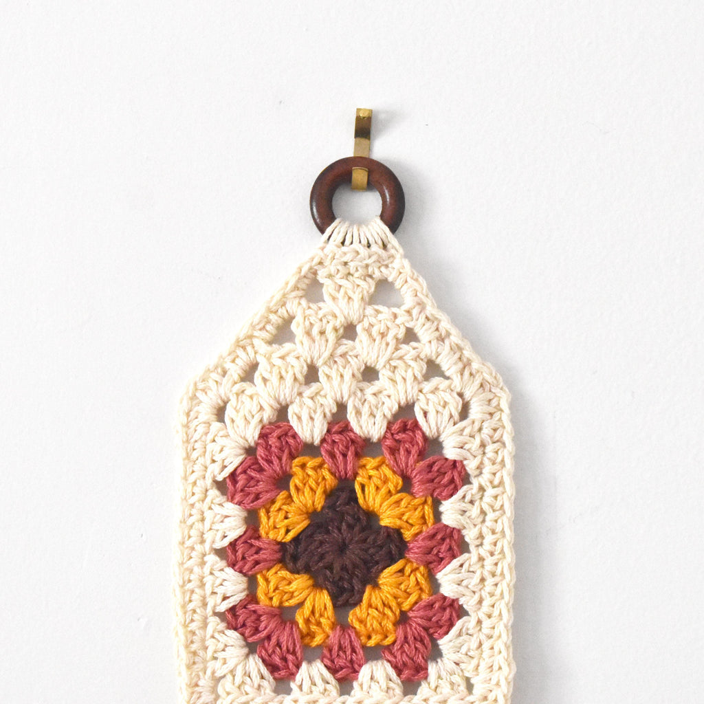 Crocheted wall hanging with a wooden ring on a white background.