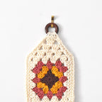 Crocheted wall hanging with a wooden ring on a white background.