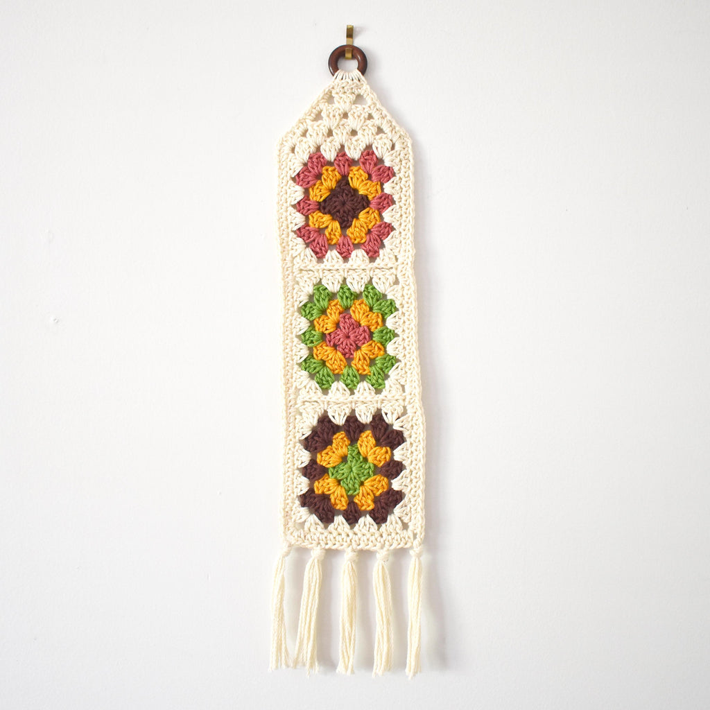 Crocheted wall hanging with multicolor granny square designs on a white background.