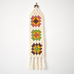 Crocheted wall hanging with multicolor granny square designs on a white background.