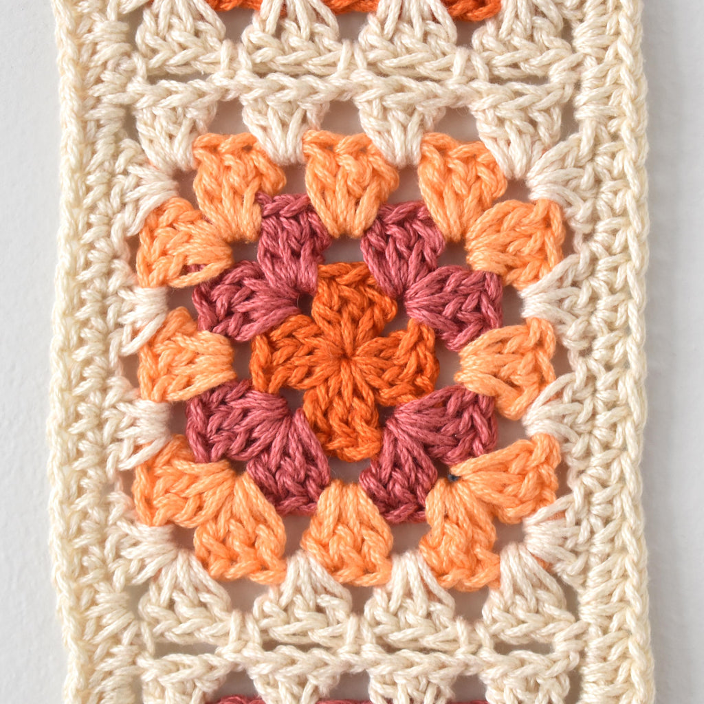 Crocheted granny square pattern in orange and pink on a white background.