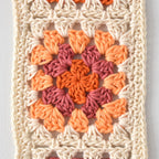 Crocheted granny square pattern in orange and pink on a white background.