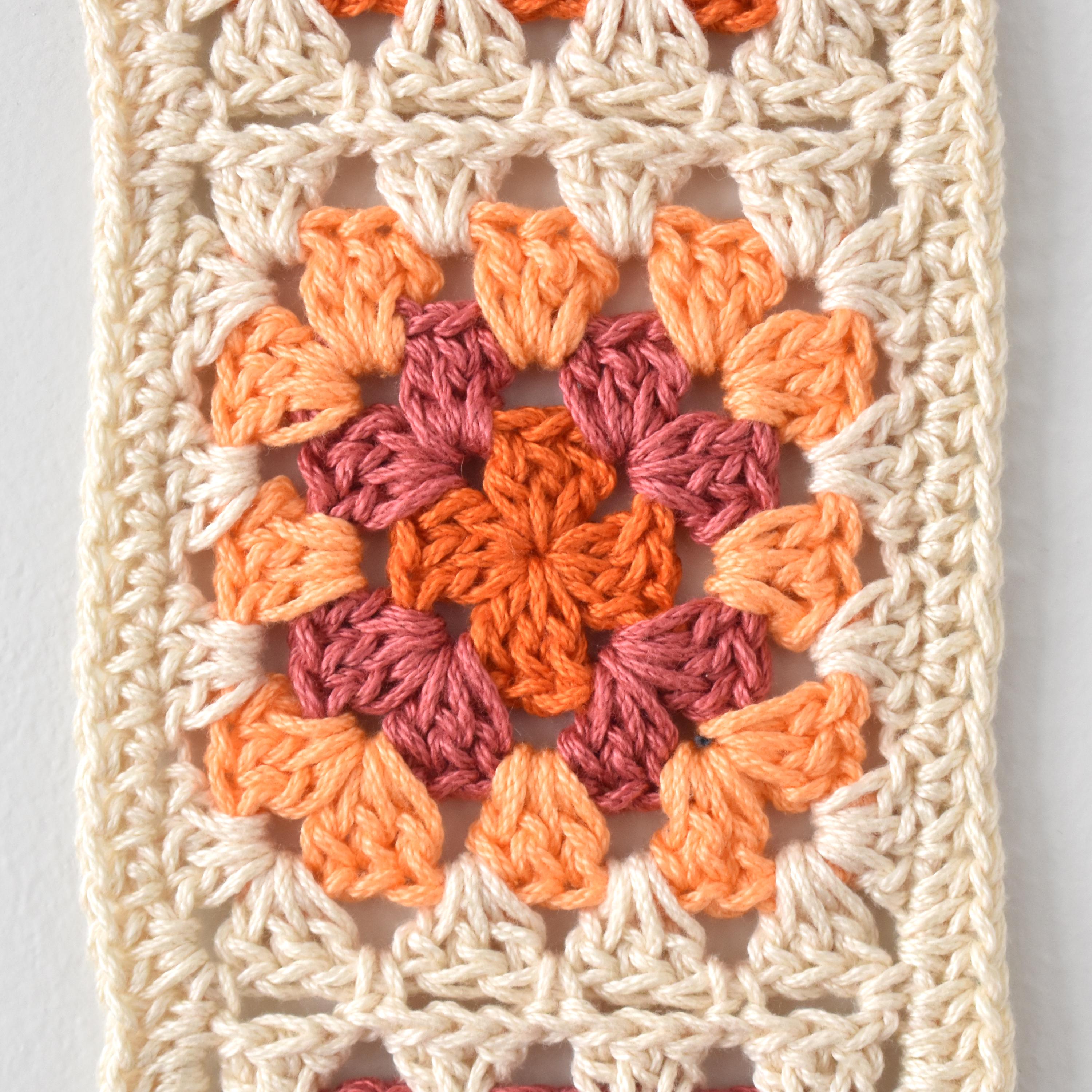 Crocheted granny square pattern in orange and pink on a white background.