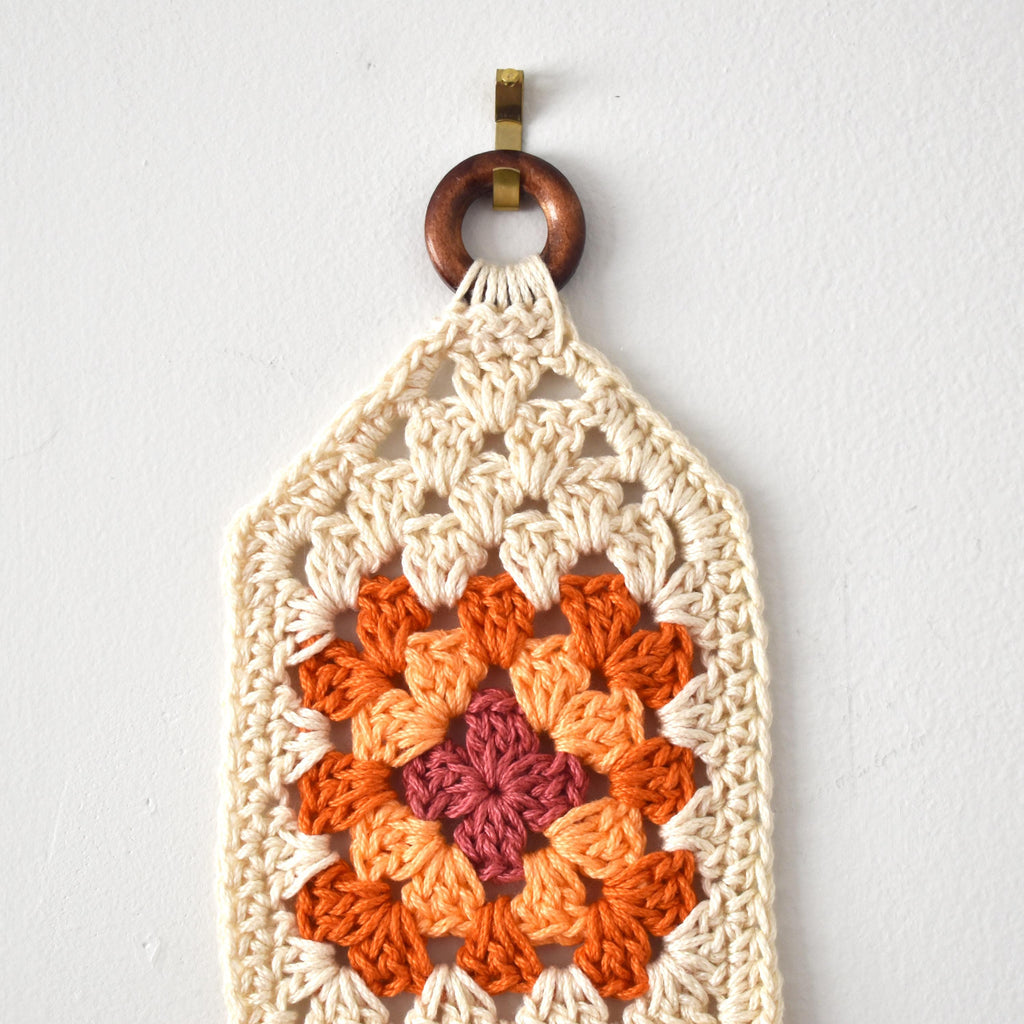 Crocheted wall hanging with a wooden ring on a white background.