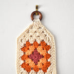 Crocheted wall hanging with a wooden ring on a white background.