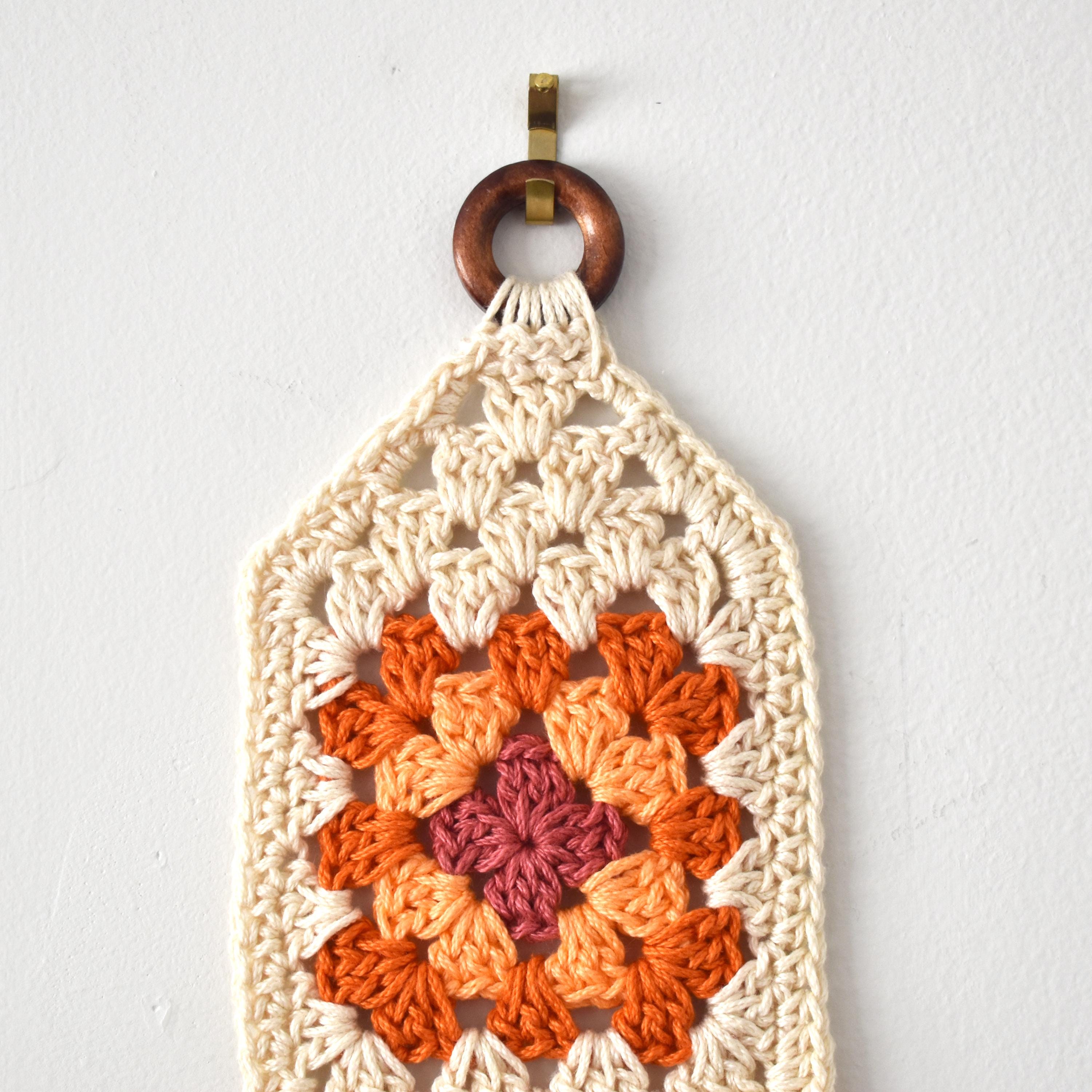 Crocheted wall hanging with a wooden ring on a white background.