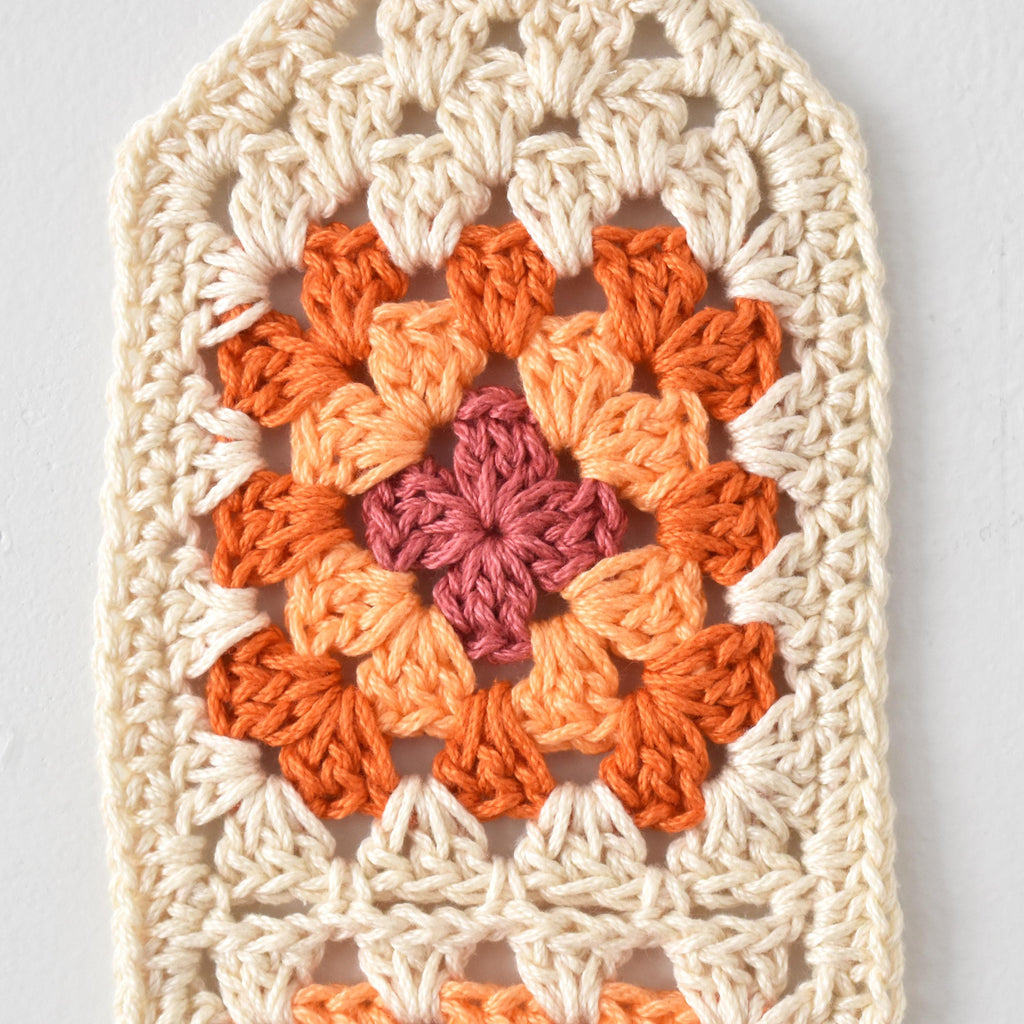 Crocheted square with a colorful granny square pattern on a light gray background.