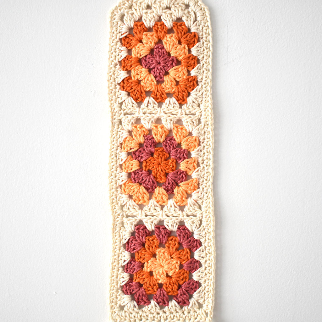 Crocheted wall hanging with a geometric pattern on a white background.