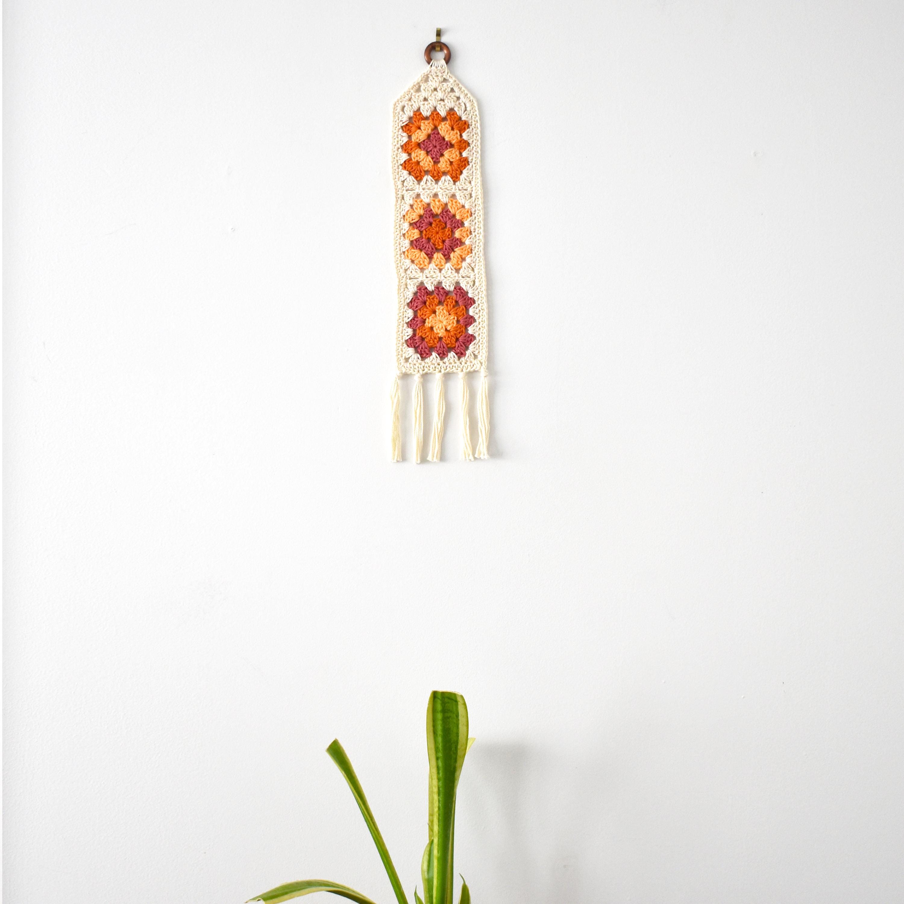 Crocheted wall hanging with geometric pattern on a white background.
