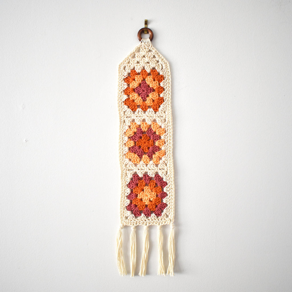 Orange crocheted wall hanging with a geometric pattern on a white background.