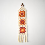 Orange crocheted wall hanging with a geometric pattern on a white background.