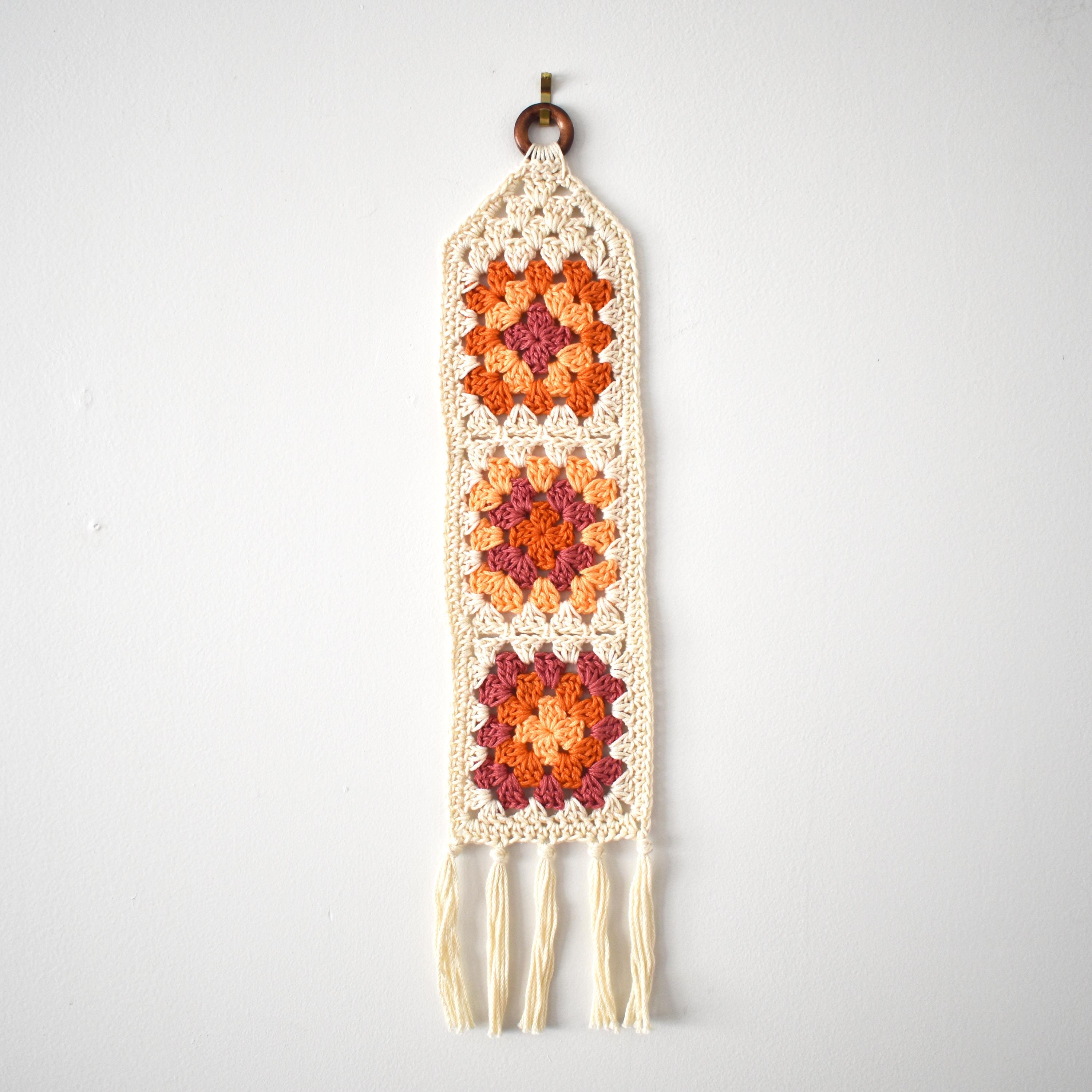 Orange crocheted wall hanging with a geometric pattern on a white background.