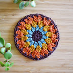 Round crochet coaster with a colorful pattern on a wooden surface.