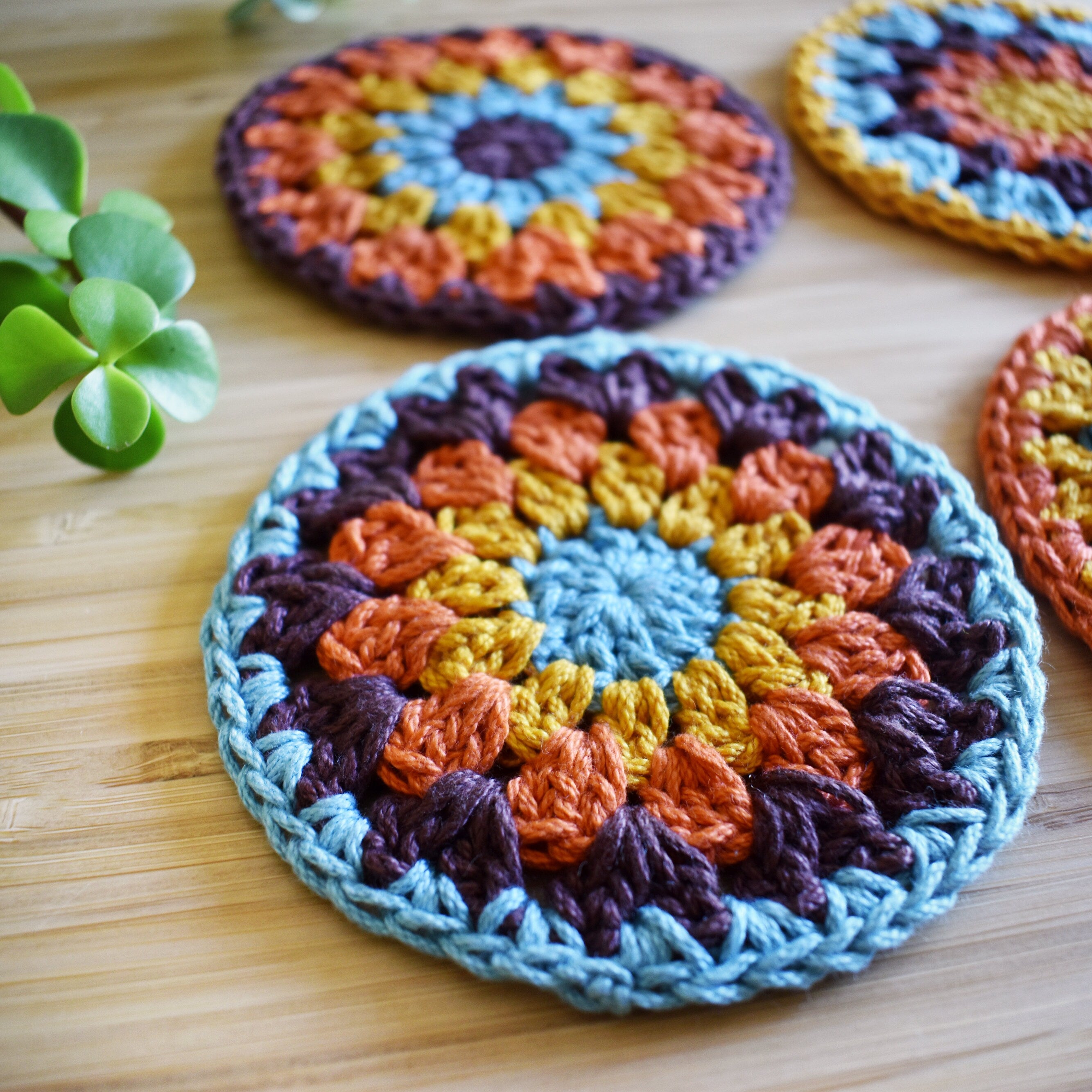 Close-up of colorful crocheted granny sunburst coasters on a wooden surface.