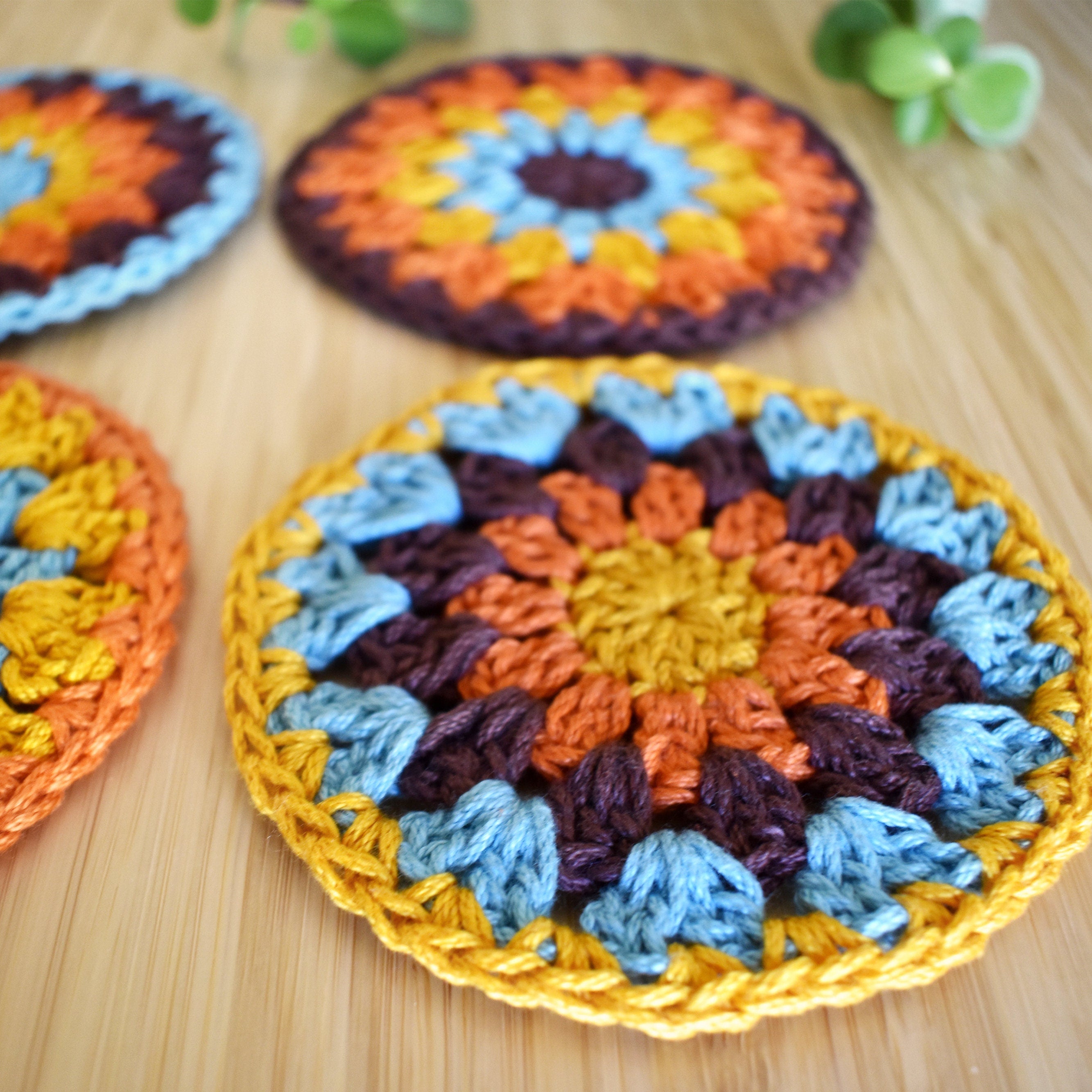 Close-up of a colorful crocheted granny sunburst coaster on a wooden surface.