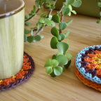 Crocheted coasters with a plant and a mug on a wooden surface.