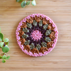 Crocheted coaster with pink and brown colors on a wooden surface.