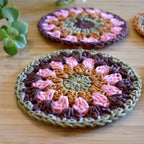 Close-up of two crocheted coasters with a granny sunburst pattern on a wooden surface.