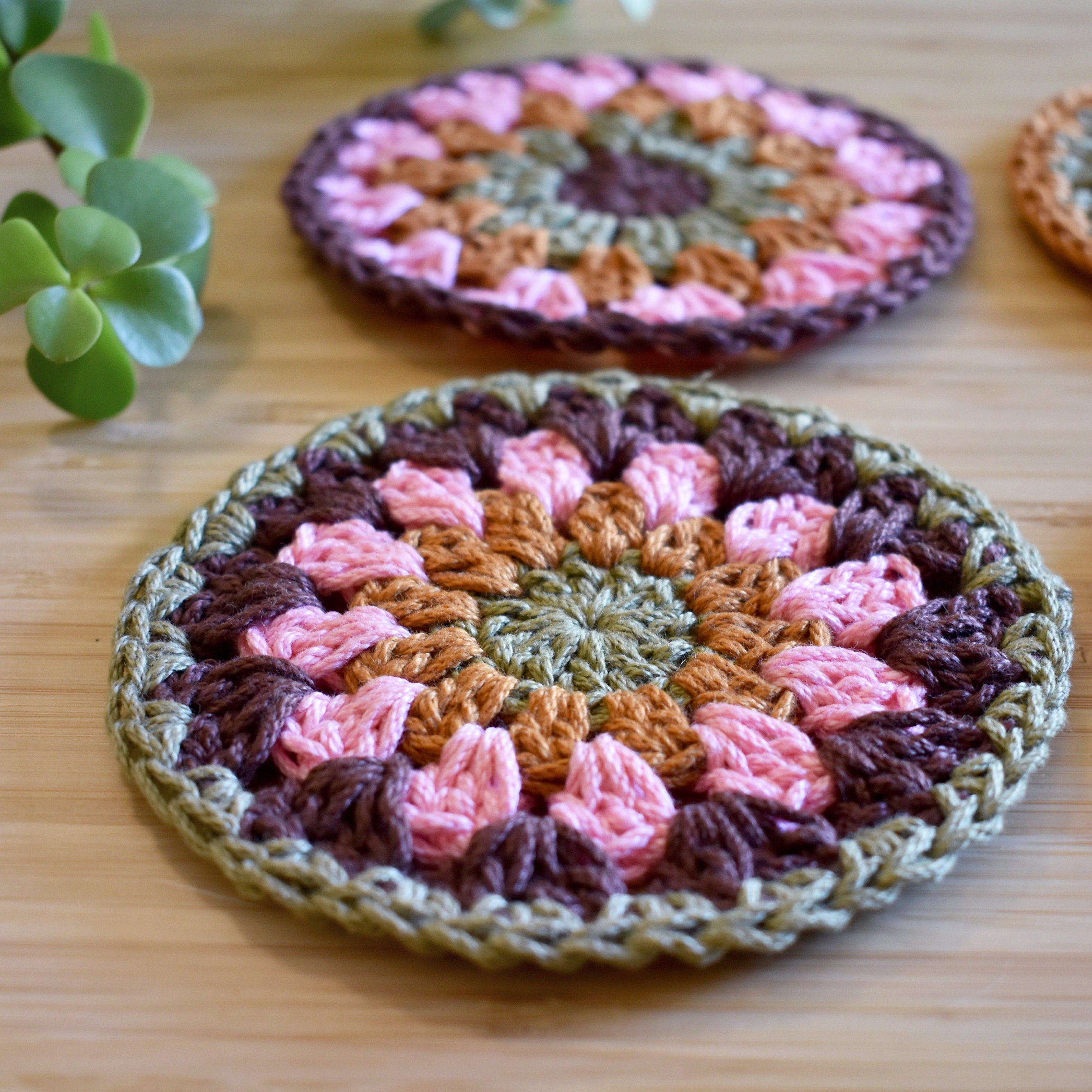 Close-up of two crocheted coasters with a granny sunburst pattern on a wooden surface.