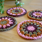Close-up of four crocheted coasters with a granny sunburst pattern on a wooden surface.