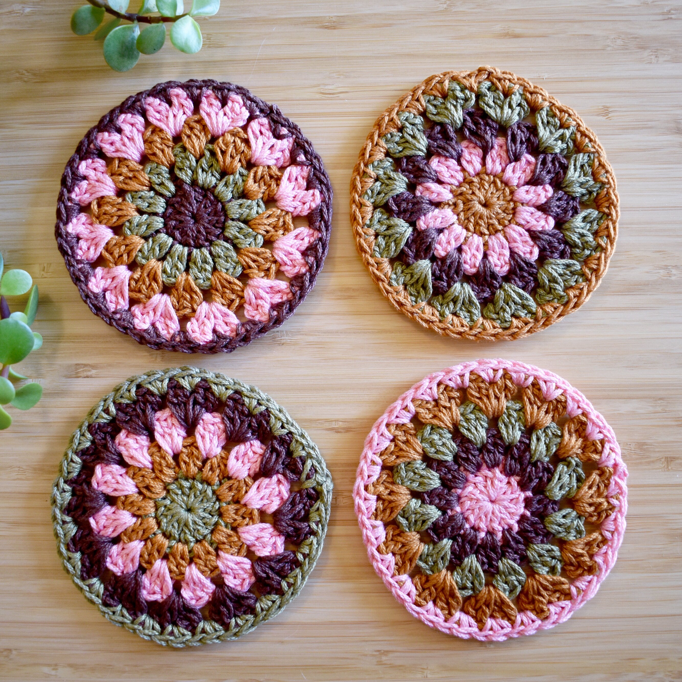 Four colorful crocheted coasters with a granny sunburst pattern on a wooden surface.
