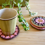 Ceramic cup with a colorful crocheted coaster on a wooden surface with a plant in the background.