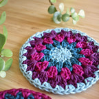 Crocheted coaster with a granny sunburst pattern on a wooden surface.