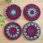 Four colorful crocheted coasters with a granny sunburst design on a wooden surface.