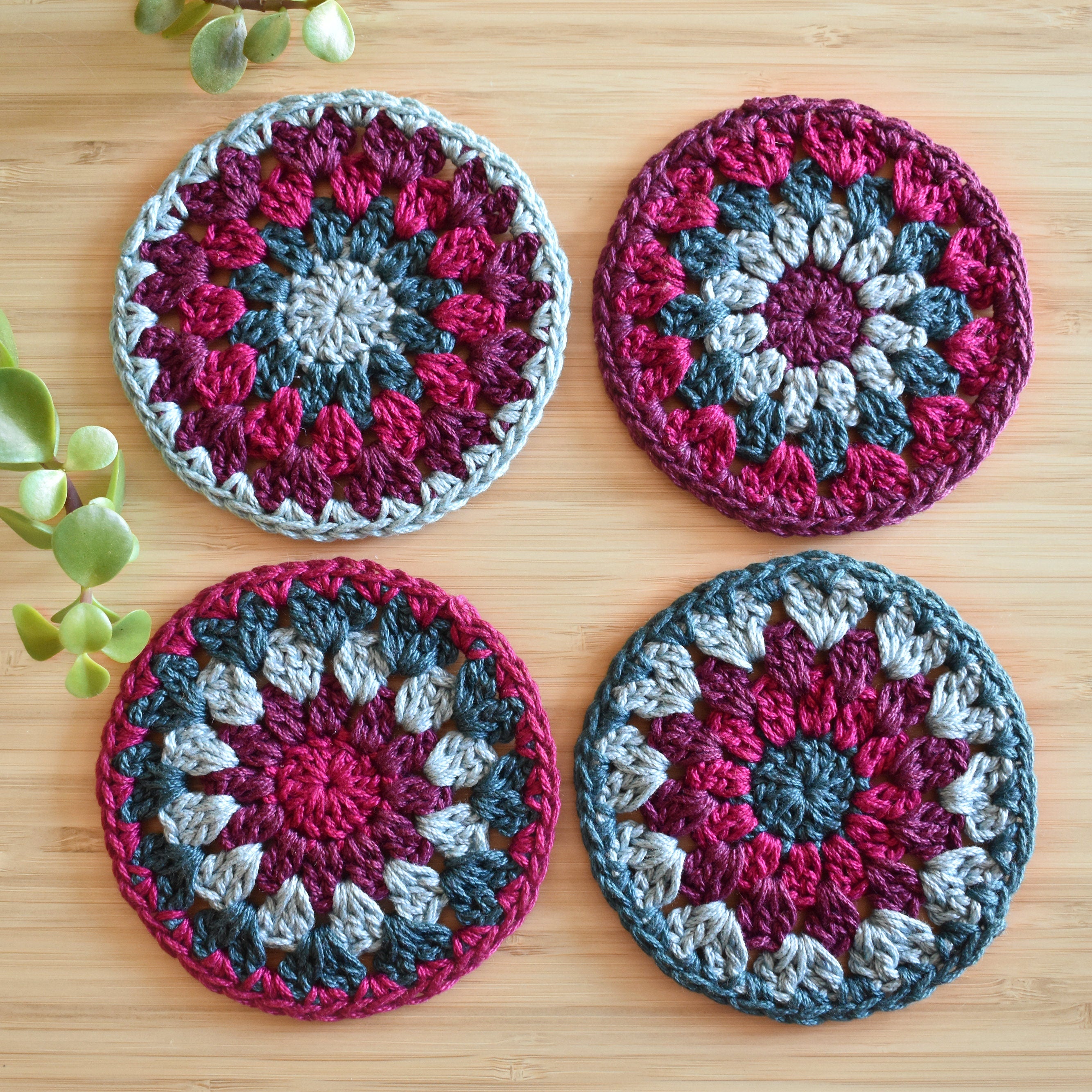 Four colorful crocheted coasters with a granny sunburst design on a wooden surface.