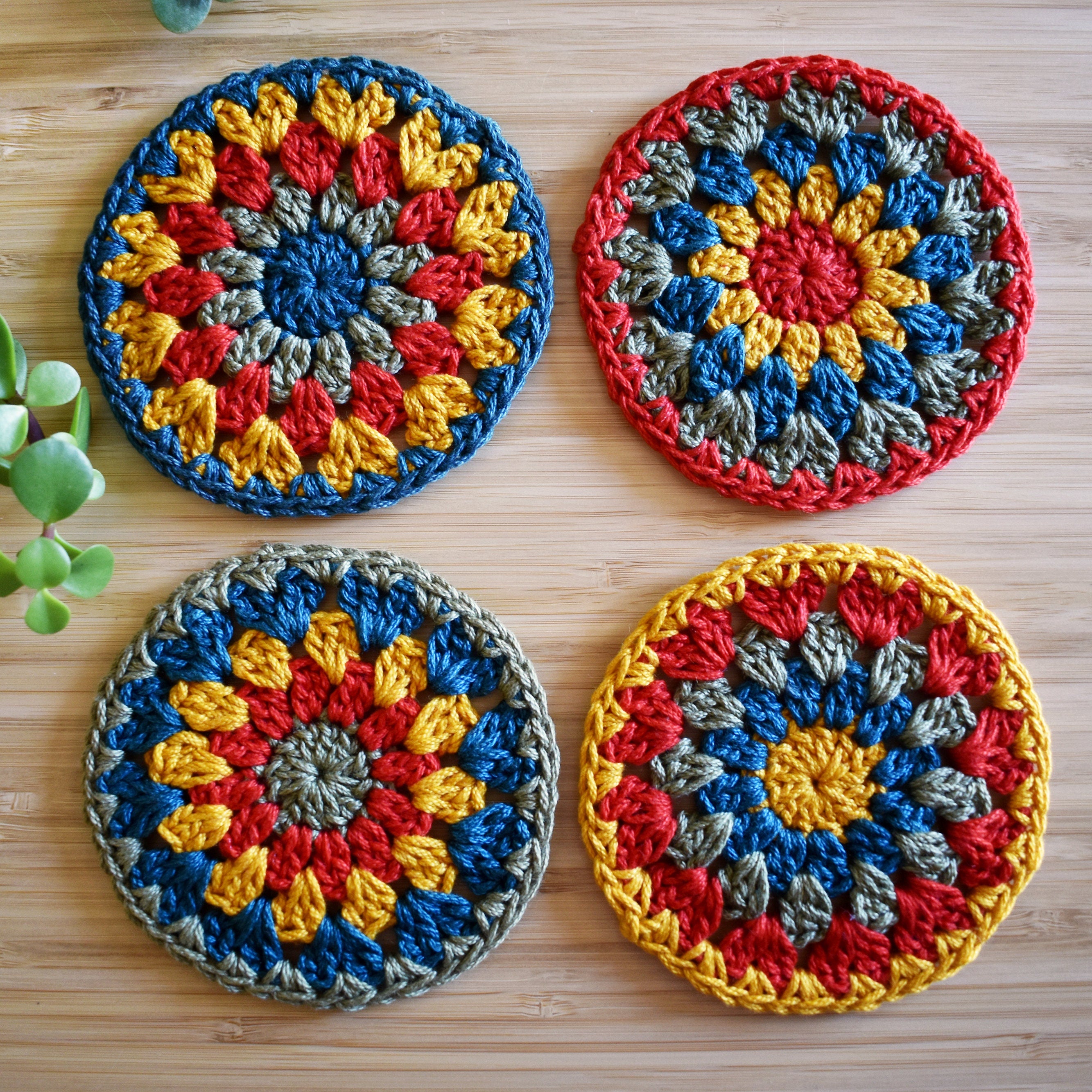 Four colorful crocheted granny sunburst coasters on a wooden surface.