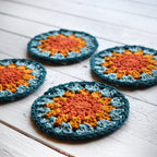 Four crocheted coasters with a granny sunburst design on a wooden surface.