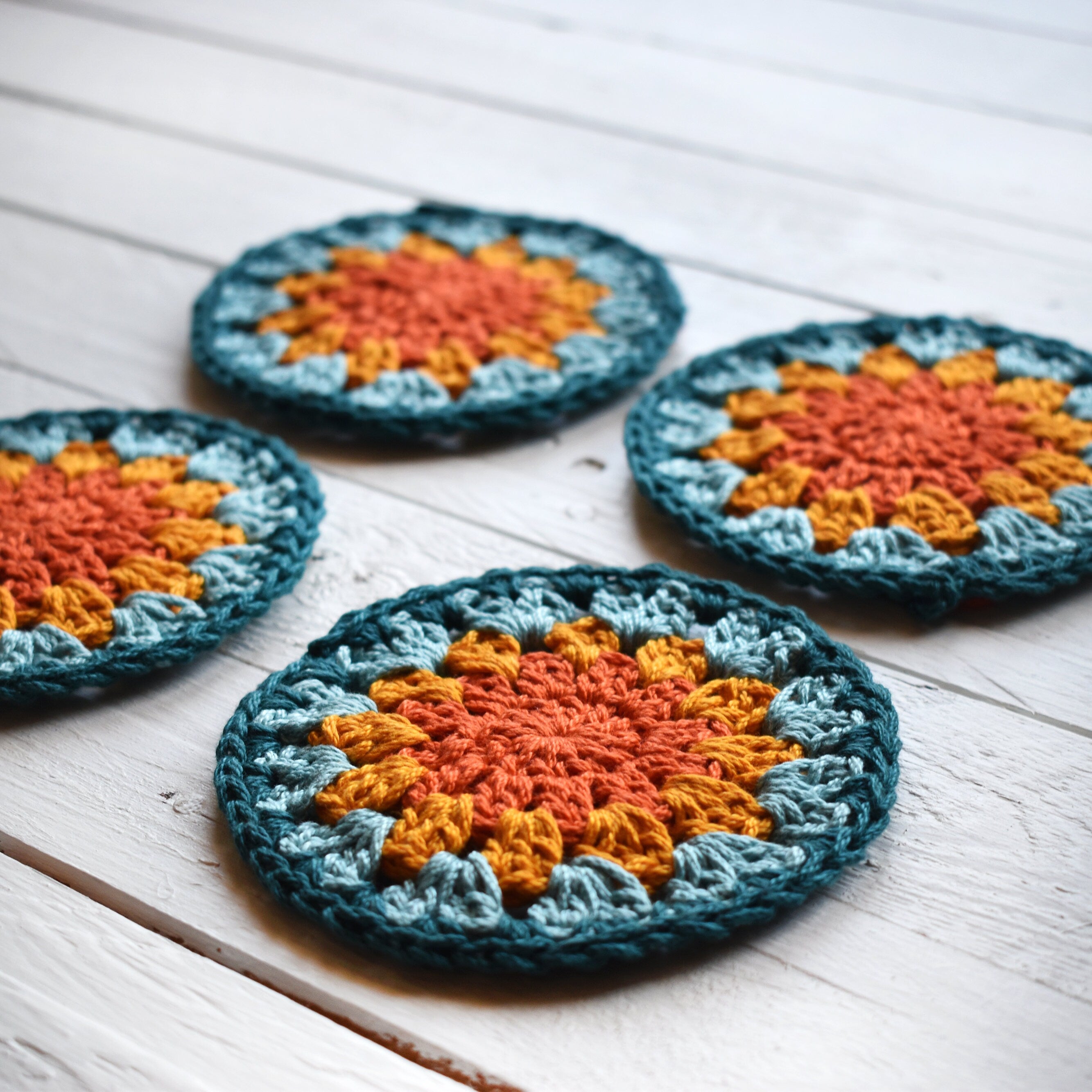 Four crocheted coasters with a granny sunburst design on a wooden surface.