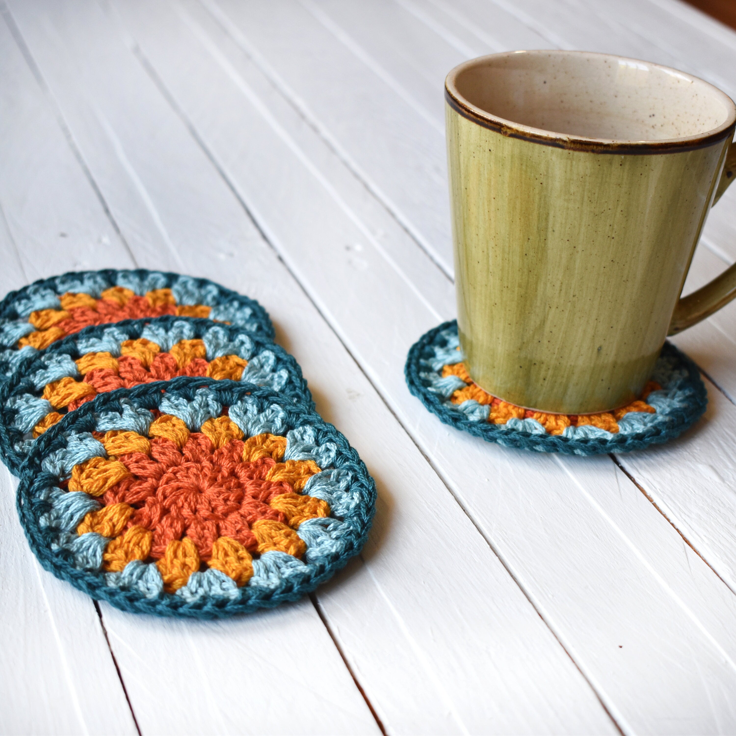 Crocheted coasters with a mug on a white wooden surface.