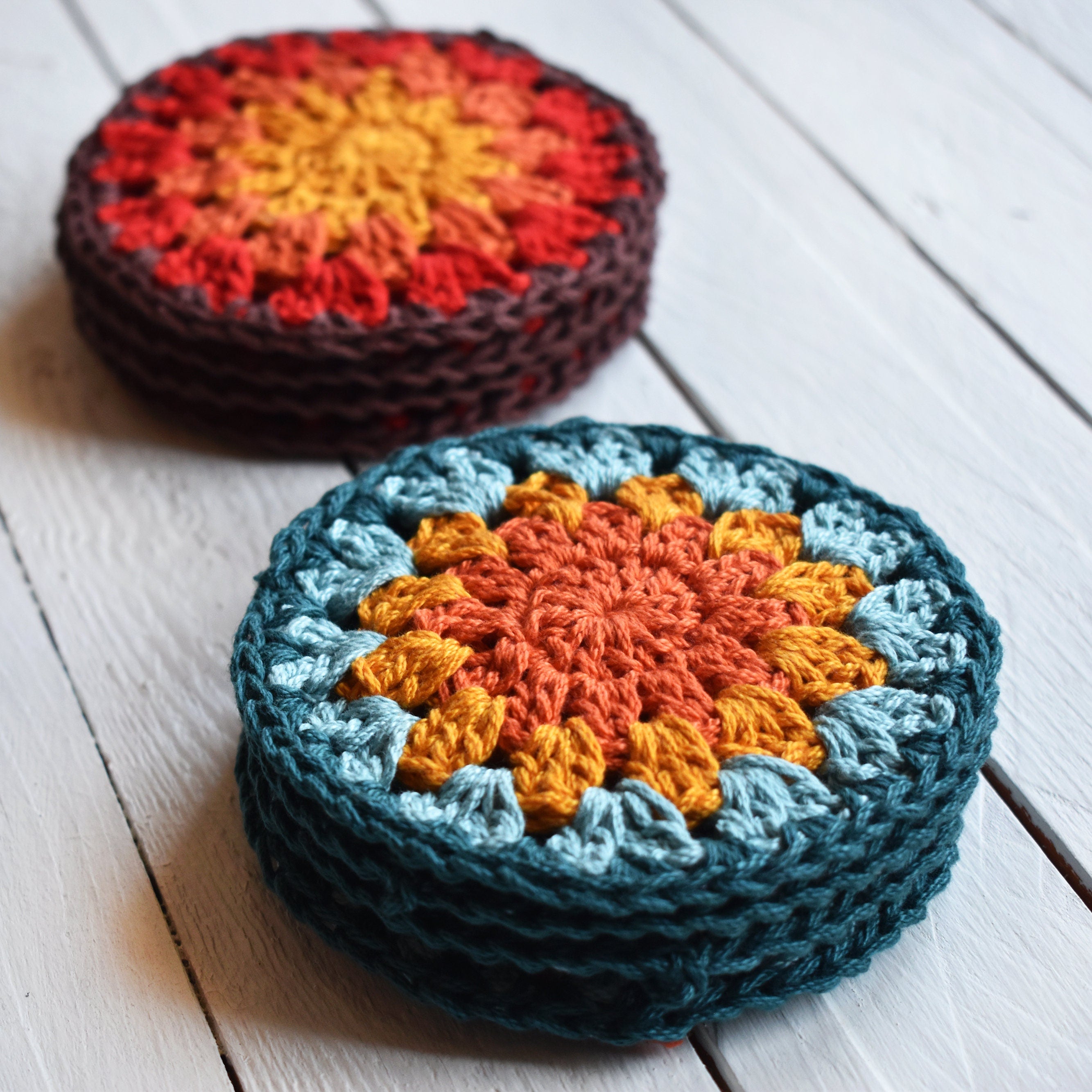 Two stacks of crocheted coasters with a sunflower design on a white wooden surface.