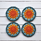 Four crocheted granny sunburst coasters with a sunrise color pattern on a wooden surface.