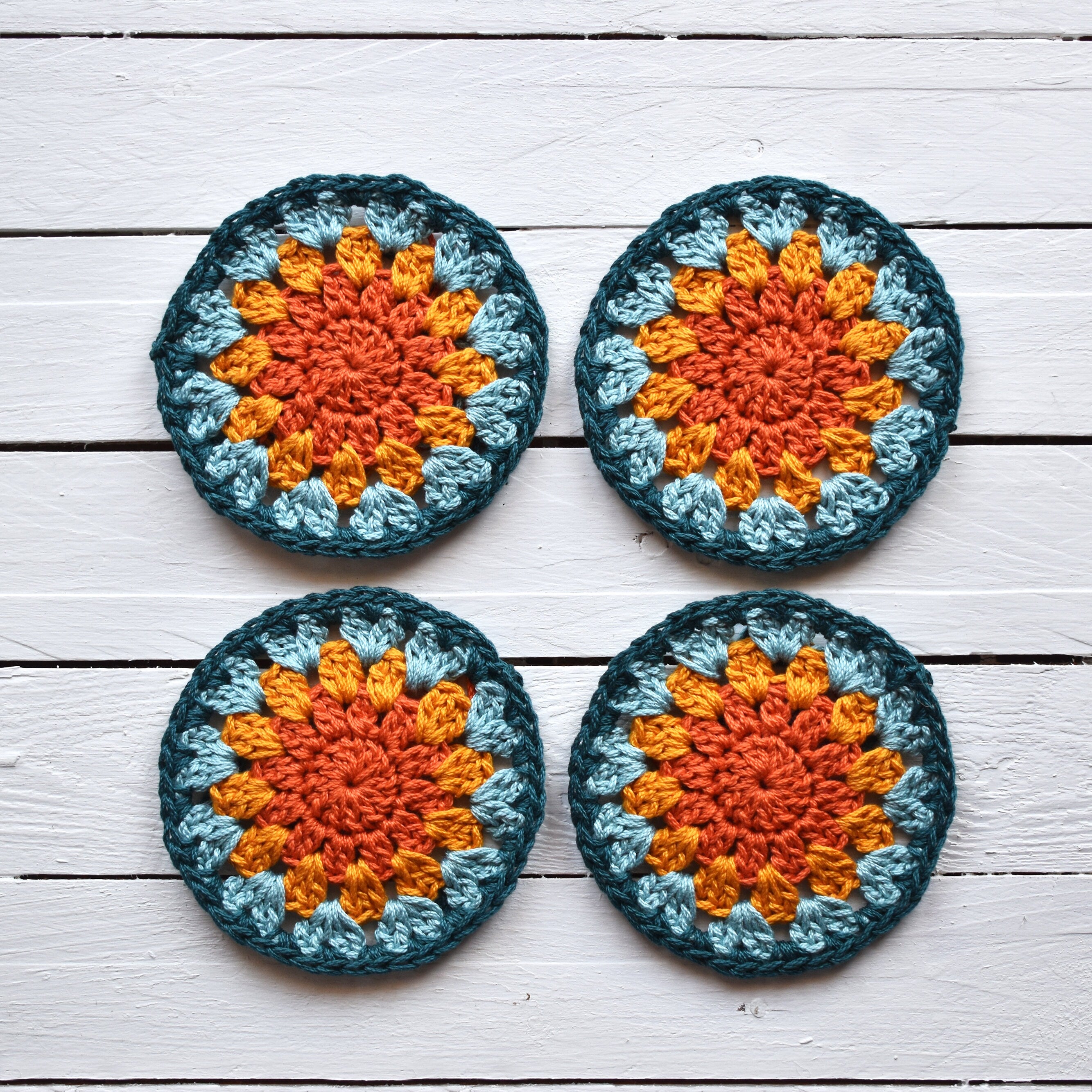 Four crocheted granny sunburst coasters with a sunrise color pattern on a wooden surface.