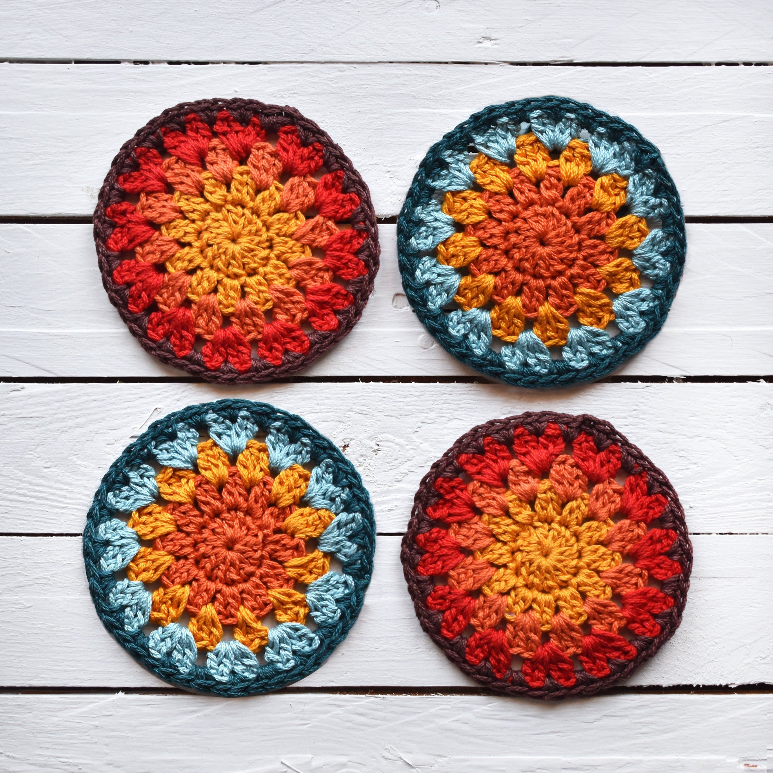 Four colorful crocheted sunburst coasters on a white wooden pallet.