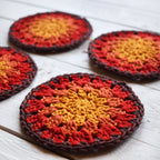 Four crocheted coasters with red, orange, and yellow colors on a white wooden surface.