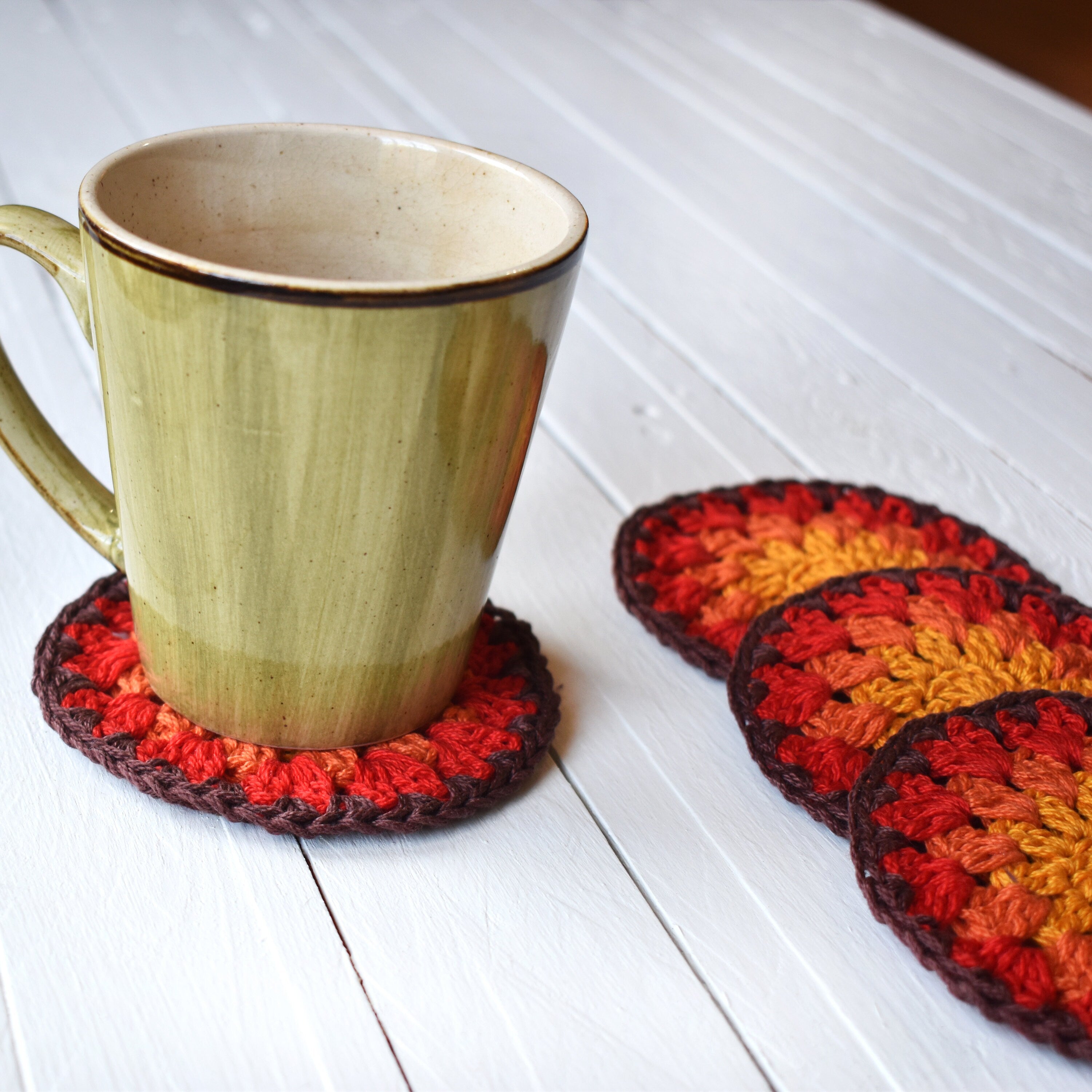 Mug with a colorful crocheted coaster on a white wooden surface.