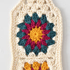 Crocheted square with a colorful flower design in the center on a white background.