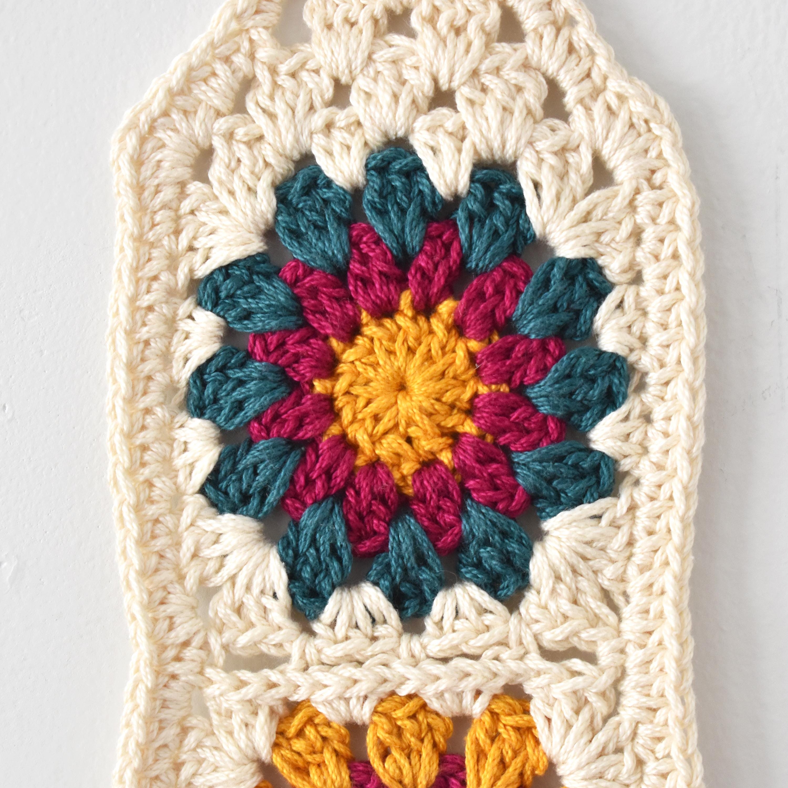 Crocheted square with a colorful flower design in the center on a white background.