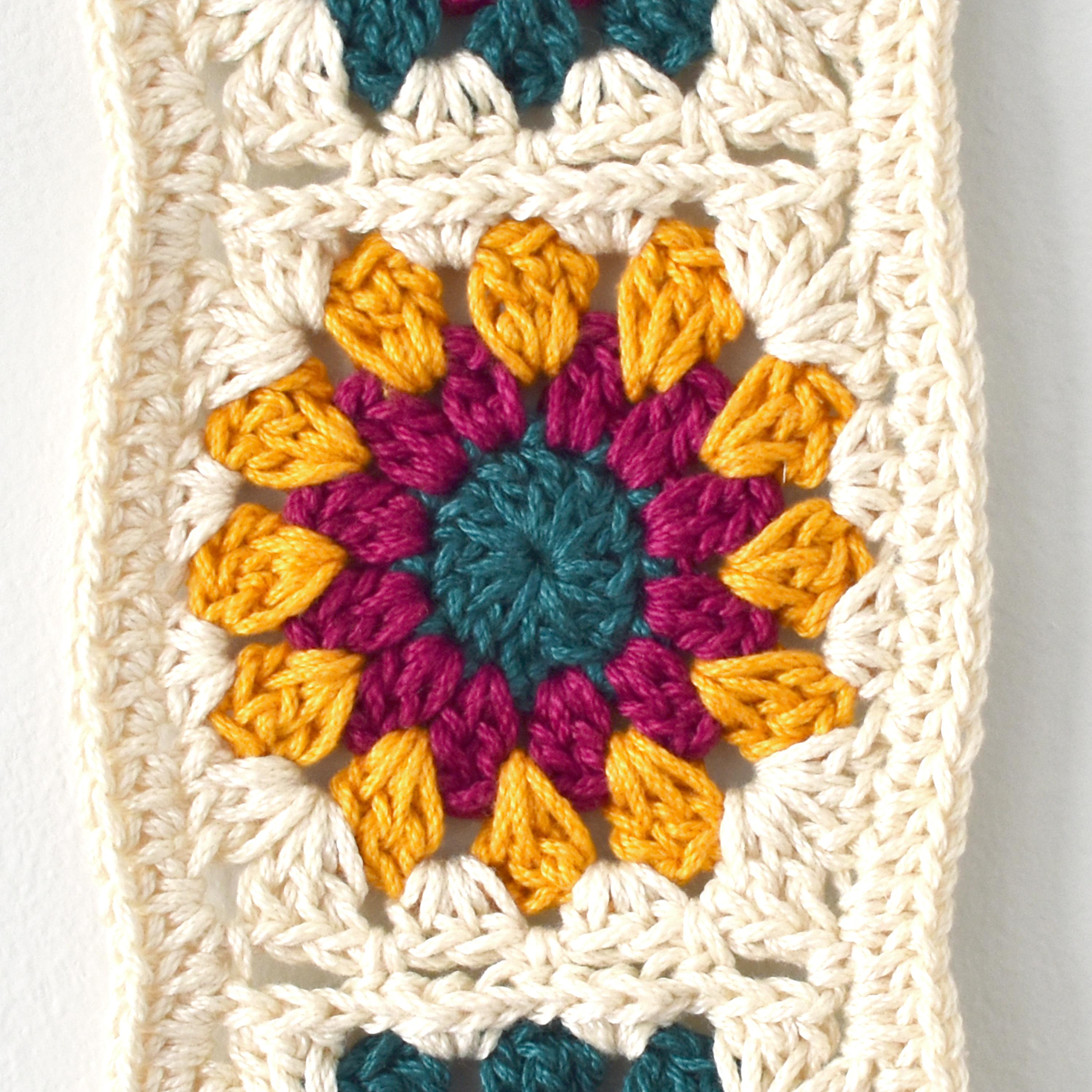 Colorful crocheted square with a floral pattern on a white background.